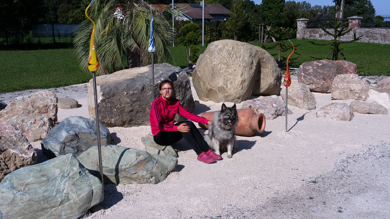 Frau mit Hund sitzt im Ausstellungspark mit vielen großen Steinen