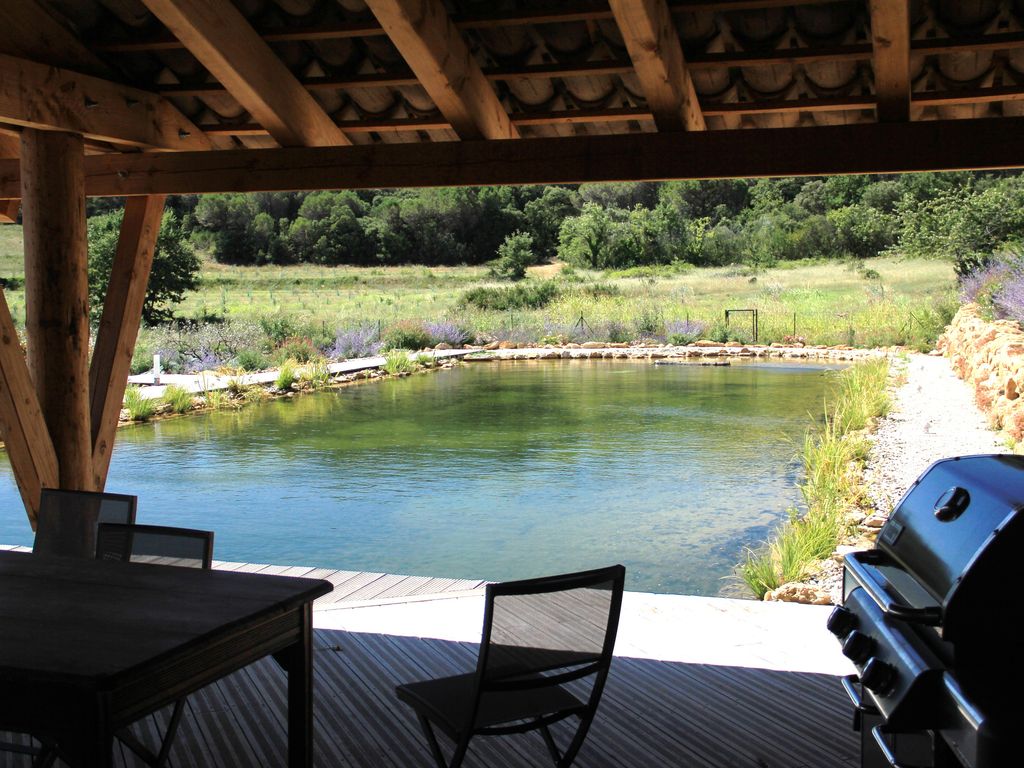 Schwimmteichanlage in Frankreich mit Findlingen im Wasser und Grillplatz auf Holzsteg